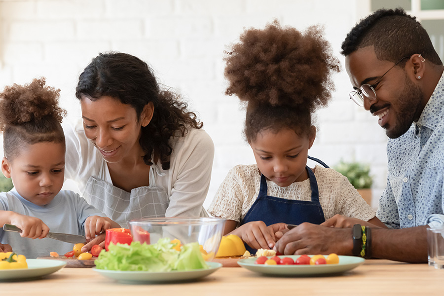 Employee Benefits - Loving Young Parents Preparing Healthy Food Salad With Little Kids in Kitchen